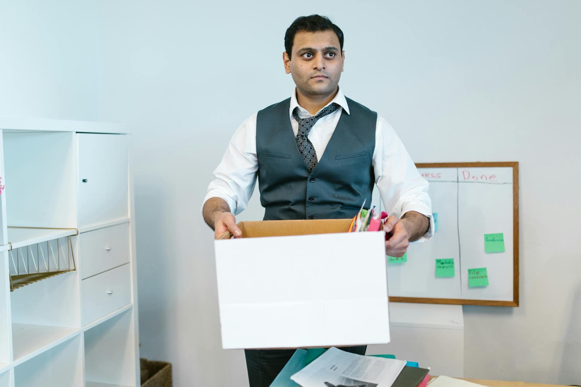 Agency founder reviewing redundancy paperwork in a modern UK office, with a packed box and travel documents visible on the desk